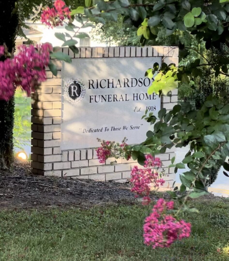 A sign for richardson funeral home with flowers in the background.